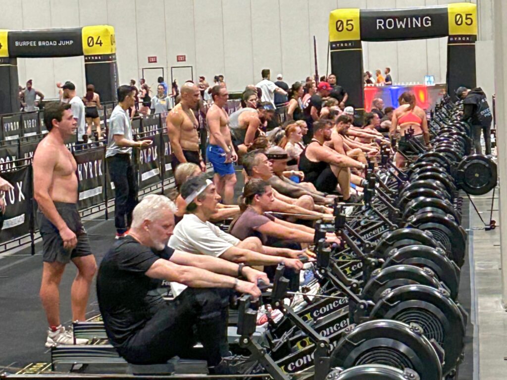 Rows of athletes on Concept2 rowing machines at the rowing station of a HYROX race