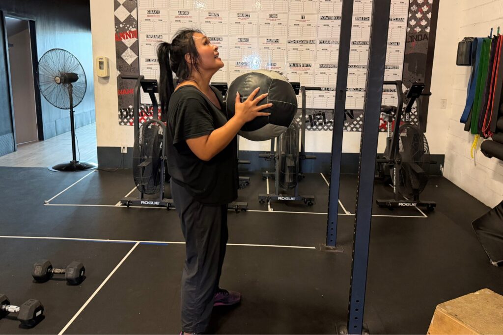 Member holding a medicine ball in front of the Cristini Athletics programming whiteboard