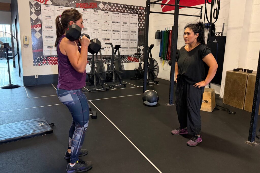 Cristini Athletics coach watching a member hold dumbbells in the front rack position